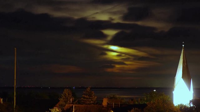 Mondaufgang hinter Wolken nahe des Kirchturmes auf Amrum