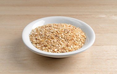 Dried minced garlic in a small bowl atop a wood table. 