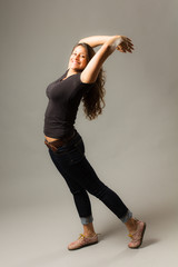 Young mixed race woman wearing a black t shirt and jeans stands with arched back while smiling at viewer