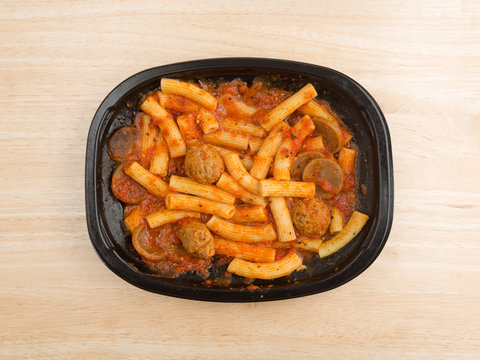 Top view of a rigatoni pasta with meatballs and sausage TV dinner atop a wood table. 