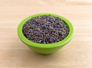 Bowl of dried lavender flower petals on a wood table.