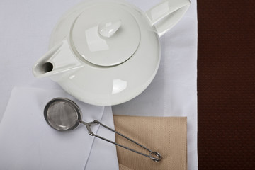 top view of a white teapot and tea strainer on a linen tablecloth