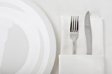 top view of empty plate, fork and knife on a white linen tablecloth
