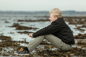 Smiling teen boy sitting on beach during low tide