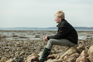 Side view of single blond boy sitting on beach