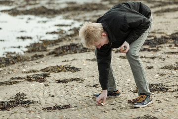 Single teen picking up stone on beach