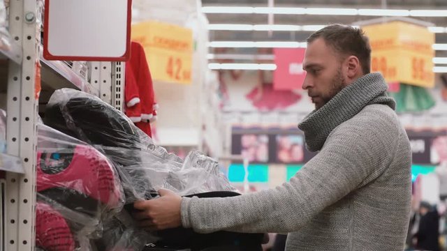 Young man choosing the item on the shelves in the store, wants to bye baby car chair, check quality. 4K