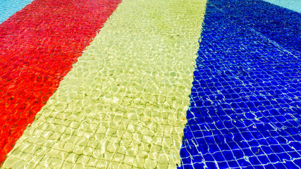 Light blue, red, yellow and blue striped mosaic floor of fountain covered with clear water at sunny...