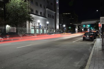 View of a busy city street at night showing cars zipping through shot at night from the sidewalk at night as long exposure, landscape composition