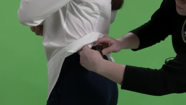 Woman wearing wireless lavalier microphone transmitter under clothing before an interview in virtual green chroma key studio