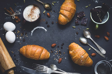 Fresh croissants, coffee, chocolate, spices and nuts on dark chalkboard background. Food still...