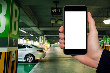 Hand with a smartphone on the background of car parking. White screen, you can insert your own...