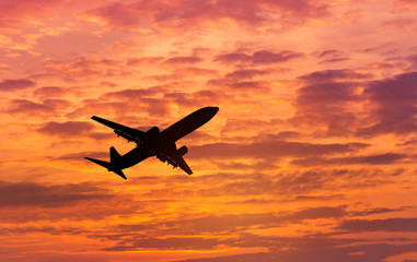 Fototapeta na wymiar Silhouette passenger airplane flying away in to sky high altitude in sunset