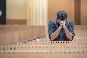 Young beard man wearing blue shirt praying in modern church - obrazy, fototapety, plakaty