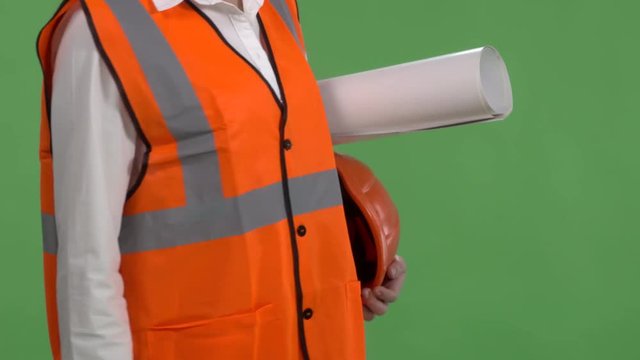 Closeup Of Female Construction Manager Or Engineer Against Green Screen. Woman In Orange Safety Vest Holding Blueprint And Hard Hat.