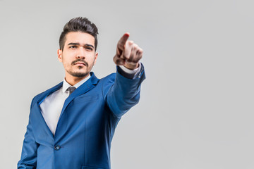 Young attractive man in a blue suit showing a finger forward on a gray background. Isolated