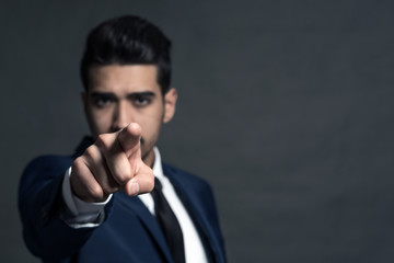 Young attractive man in a blue suit showing a finger forward on a gray background