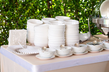 Fototapeta na wymiar Ceramic white plate stacked on table for party in shady garden