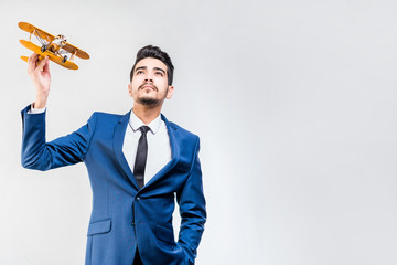 Young attractive man in a blue suit holding a yellow airplane model on a gray background. Isolated