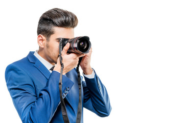 Young attractive man in a blue suit with a camera on a white background. Isolated