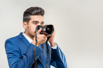 Obraz premium Young attractive man in a blue suit with a camera on a gray background