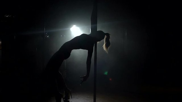 One caucasian woman pole dancer dancing in silhouette studio, slow motion.
