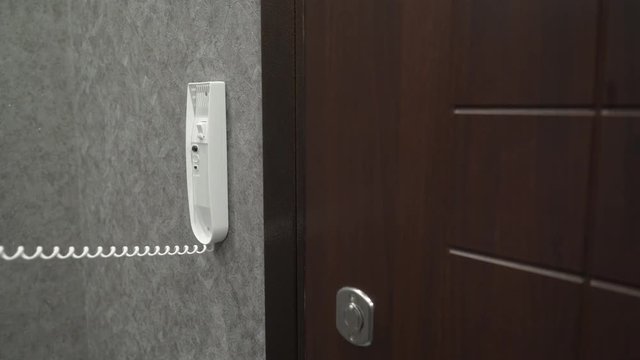 Person holding handset of intercom system installed on a wall in the apartment answering a call