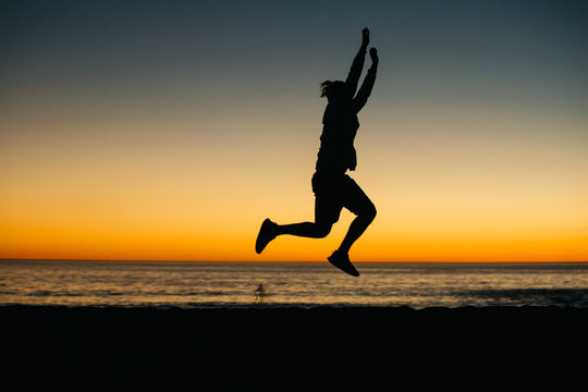 Silhouette of a happy man athlete celebrating winning success at sunset or sunrise elated with arms above his head in celebration reached his goal during hiking travel trek.