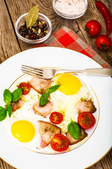 Fried eggs with bacon and vegetables on a white plate