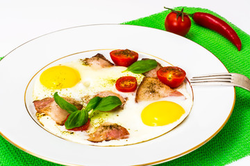 Fried eggs with bacon and vegetables on a white plate
