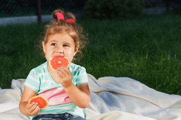 Small girl holds a slice of fresh grapefruit