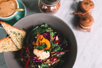 Close up og the dish with vegetarian salad with red pepper, cabbage, onion, lettuce, seeds and hummus on a marble table