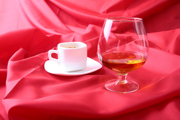 White cup of coffee and cognac in a glasses, pralines on red background.