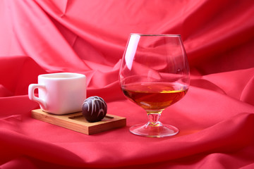 Fototapeta na wymiar White cup of coffee and cognac in a glasses, pralines on red background.
