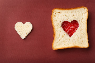 The composition of Valentine's Day. Left side: heart from white bread, the right side: sandwich with red heart of raspberry jam. All this rests on a red background.
