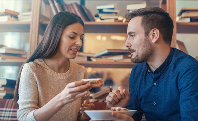 Couple in love. Young couple eating cake surrounded with books i