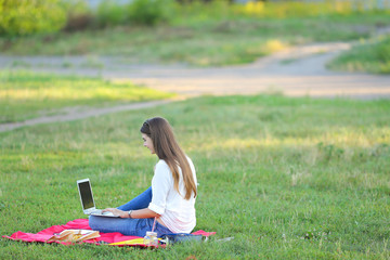 lady sitting in the park and talking on Skype via a laptop with headphones