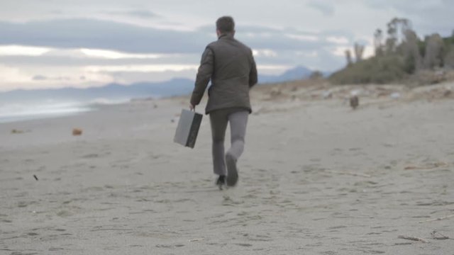 Uomo impaurito scappa sulla spiaggia con la valigetta