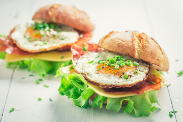 Homemade burger with lettuce, bacon and eggs on white table