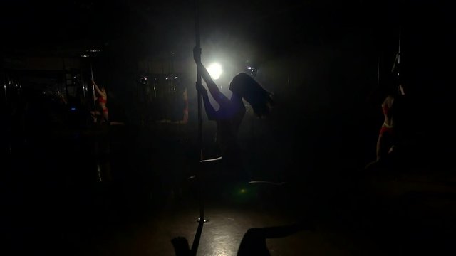 Sexy girl spinning around a pole in a dark room in slow motion. Pole dance.
