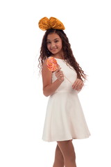Lovely girl brunette with long hair in a white dress with a bow on her head with a big candy on a...