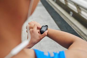 Close-up shot of young sportsman in blue T-shirt checking his heart rate on fitness tracker, over the shoulder view