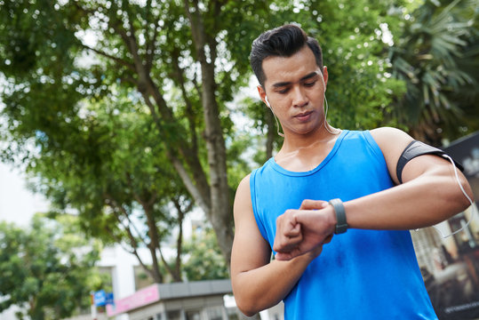 Portrait of modern young sportsman in blue T-shirt using gadgets during training in summer park