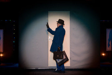 Male actor in a blue suit plays a role in the background of a theater stage with scenery for the play. © Kozlik_mozlik