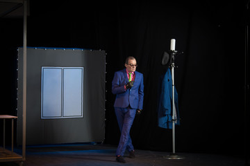 Male actor in a blue suit plays a role in the background of a theater stage with scenery for the...