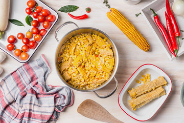 Corn cooking preparation with ingredients with pot and ear on white wooden kitchen background, top view