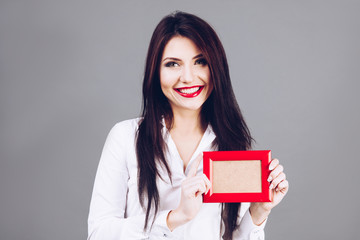 Beautiful brunette girl holding red photo frame in hands.