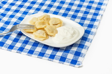 dumplings on a plate with sour cream and a fork on a blue tablecloth