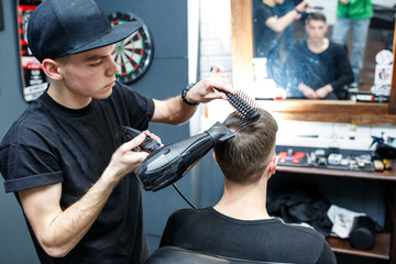 Master cuts hair of men in the barbershop, hairdresser makes hairstyle for a young man