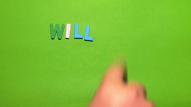 Wood characters of different colors arranged in a word will you marry me on a green background with hand slide

